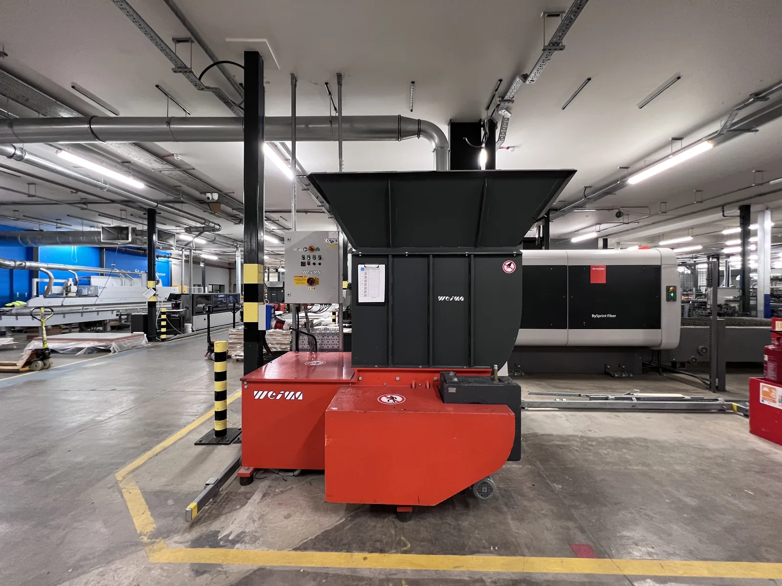 Factory interior with machinery, overhead services and linear lighting.