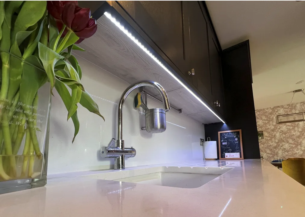 Linear LED lighting beneath dark kitchen wall cabinets.